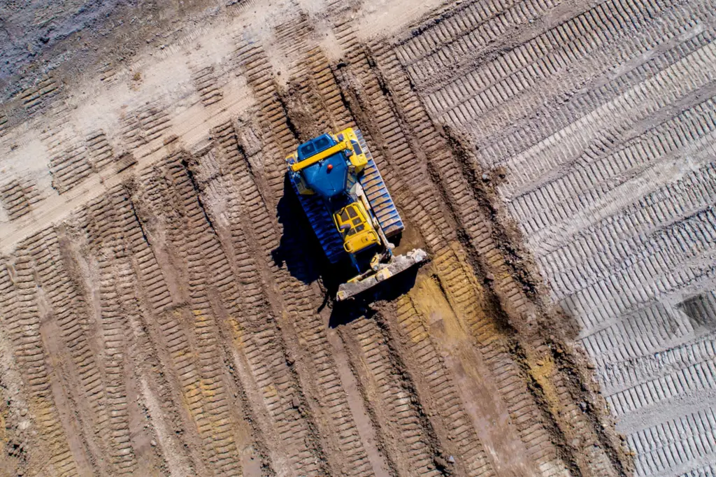 Aerial view of a bulldozer grading and leveling soil at a construction site.